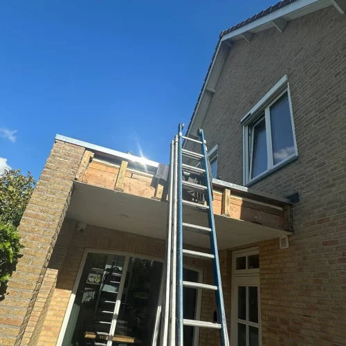 Opengewerkte dakrand van een aanbouw met ladder tegen de gevel in Barneveld